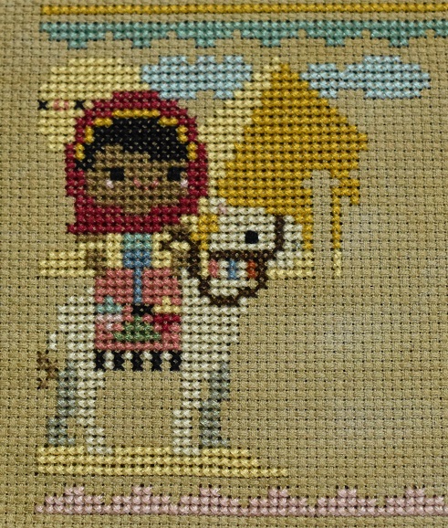 Cross stitch scene of a girl riding a camel past a pyramid